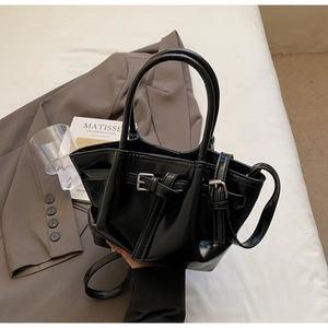 Détail du sac seau noir en cuir brillant avec boucle sur fond de costume gris chic