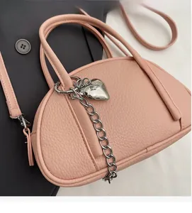 Détail du sac à main rose en cuir grainé avec chaîne argentée et pendentif cœur