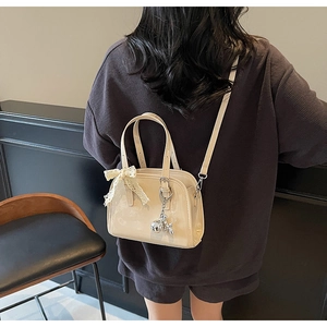 Glossy patent leather Boston bag with lace bow detail and metallic charm on a model
