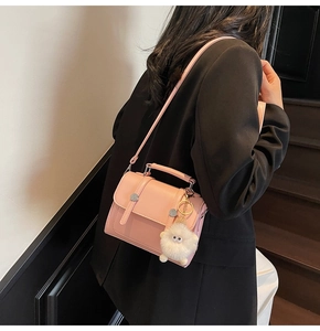 Detail of light pink crossbody bag with dual buckles and plush charm on black blazer