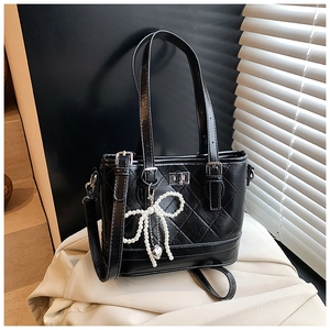 Detail of black quilted leather bucket bag with pearl bow charm and silver twist lock