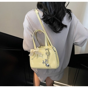 Detail of cream glossy leather handbag with lace bow and silver balloon dog charm