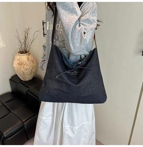 Detail of large black denim tote bag with drawstring closure and golden text print
