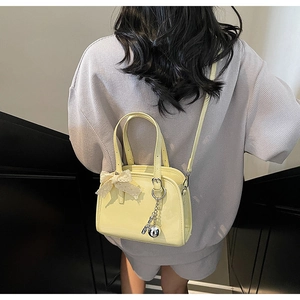 Detail of yellow patent leather Boston bag featuring lace bow and silver charm