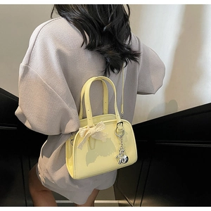 Detailed view of yellow patent leather Boston bag with lace bow and rabbit charm detail