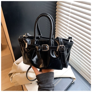 Detailed close-up of glossy black leather bucket bag with silver buckle and smooth texture