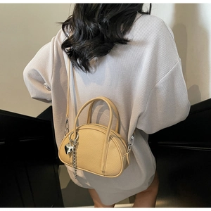 Sac bandoulière en similicuir beige avec pendentif cœur argenté porté par un mannequin