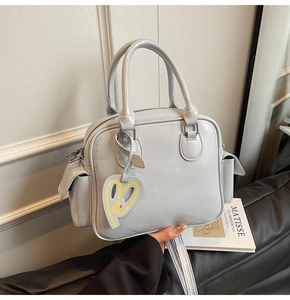 Detail view of light grey Boston tote bag with side pockets and heart charm