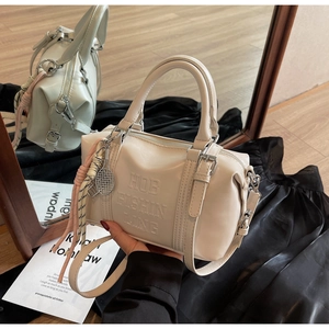 Detalle del bolso Boston crema con colgante de raqueta de tenis y cordón en suelo de madera