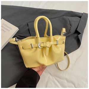 Detail of yellow bucket bag featuring decorative buckle, silver hardware and slim strap