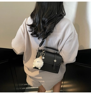 Detail of minimalist black crossbody bag with white plush charm on lavender attire