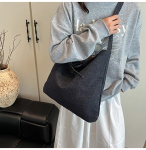 Detail of a large dark grey denim tote bag with minimalist text on casual model