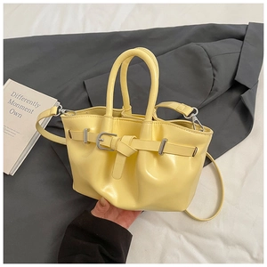 Detail view of cream bucket bag with silver buckle and removable strap on bed