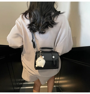 Detailed view of black matte handbag with silver buckles and a white plush pompom charm