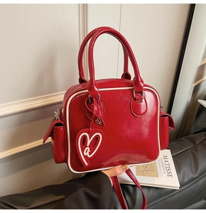 Detail of red patent leather Boston bag with white stitching and heart pendant charm
