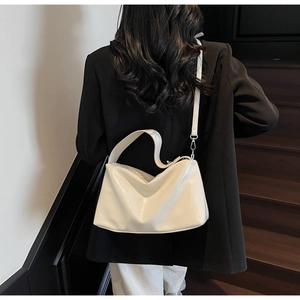 Rear view of a white glossy shoulder bag on a black blazer with wooden stairs background