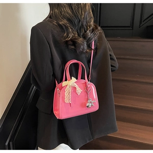 Detail of hot pink glossy leather handbag with lace bow and silver balloon dog charm