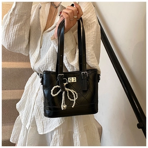 Detail of black quilted bucket bag featuring a pearl bow charm and silver square twist lock