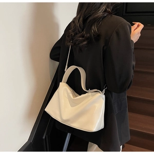 Minimalist beige leather shoulder bag featuring a wide strap shown on a model