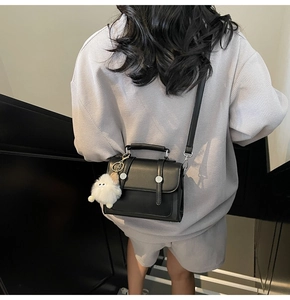 Detail view of a black vintage crossbody bag with silver buckles and plush charm on model
