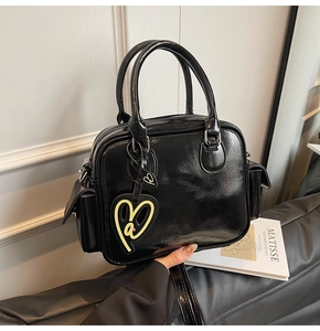 Detail of glossy black Boston tote featuring side flap pocket and yellow heart charm