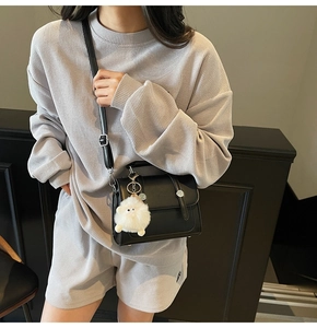 Detail of minimalist black PU leather crossbody bag with metal buttons and a plush lamb charm