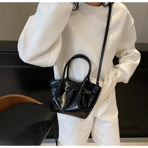 Détail d'un sac bandoulière en cuir ciré noir montrant la texture brillante et la boucle métal