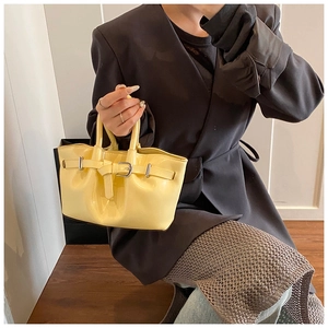 Detail of yellow patent leather handbag with soft pleats and metallic buckle accent