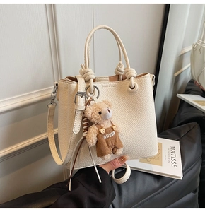 Detail of beige lychee texture bucket bag with knotted handle and plush bear charm