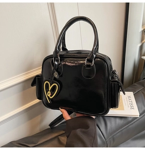 Detail of glossy black patent leather Boston tote bag with heart charm and shoulder strap