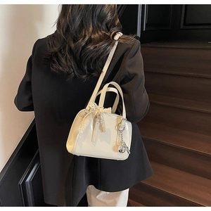 Chic cream patent leather Boston bag with lace bow and metal pendant on model
