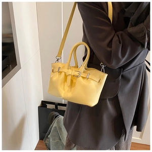 Elegant pale yellow glossy bucket bag shown being worn as a stylish shoulder accessory