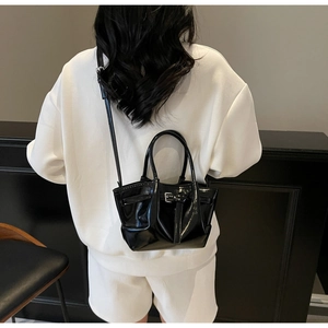 Détail du sac seau noir verni avec boucle décorative et doubles poignées de transport