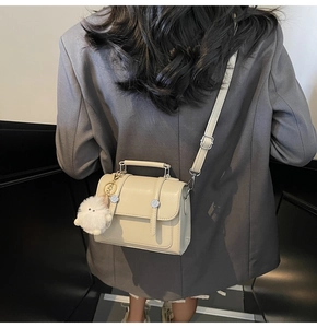 Close-up of beige crossbody square bag with top handle and plush charm on a model