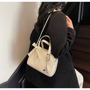 Detail of cream white glossy boston bag with lace bow and silver metal charm