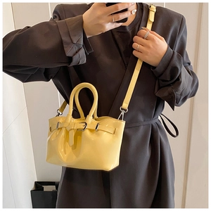 Detail of yellow glossy bucket bag with pleated texture and decorative belt strap