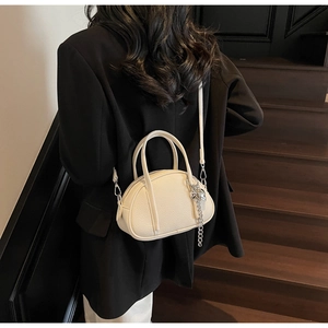 Détail du sac Boston blanc cassé avec texture litchi et breloque coeur argentée