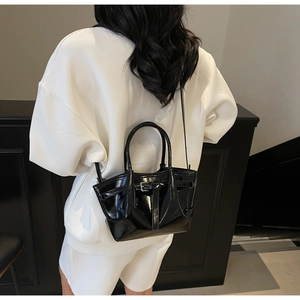 Détail d'un sac seau en cuir verni noir brillant avec poignées et bandoulière réglable