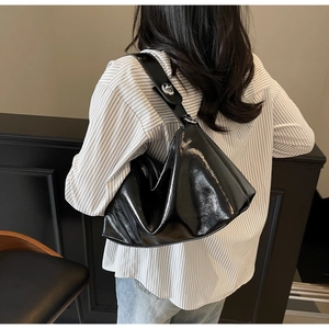 Detailed view of large black shiny shoulder bag with silver buckle and wide strap on model