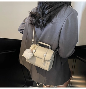Close-up of cream leather square handbag with top handle and cute fluffy chicken charm