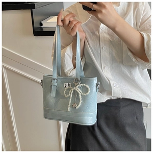 Light blue quilted bucket bag with pearl bow charm detail on a model for daily commute