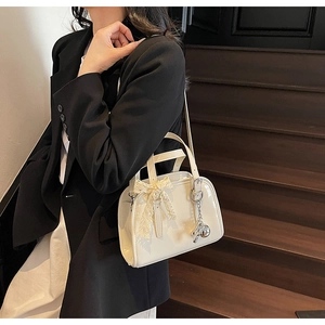 Detail of cream patent leather Boston bag with lace bow and metallic charm detail