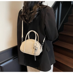 Détail du sac crème en cuir grainé avec pendentif en forme de cœur argenté et bandoulière