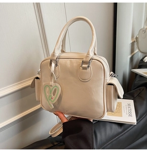 Detail of beige Boston tote bag with side flap pockets and green heart tag
