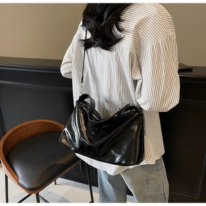 Glossy black patent leather shoulder bag with a spacious soft structure on model