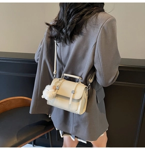 Detail of a beige leather crossbody square bag with a plush charm on a grey blazer