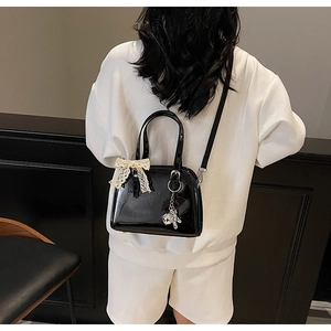 Detail of black patent leather shell bag with white lace bow and silver animal charm