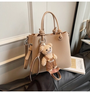 Detail of beige litchi grain tote bag with knot handle and cute bear charm accent