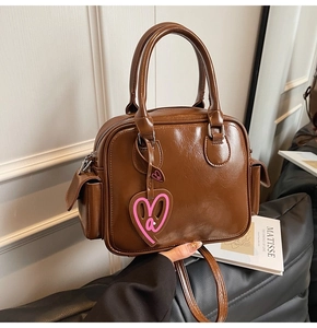 Detail of glossy brown Boston bag with double handles and a pink heart-shaped charm