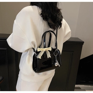 Detail of black patent leather bag with lace bow and silver sphere charm accessory